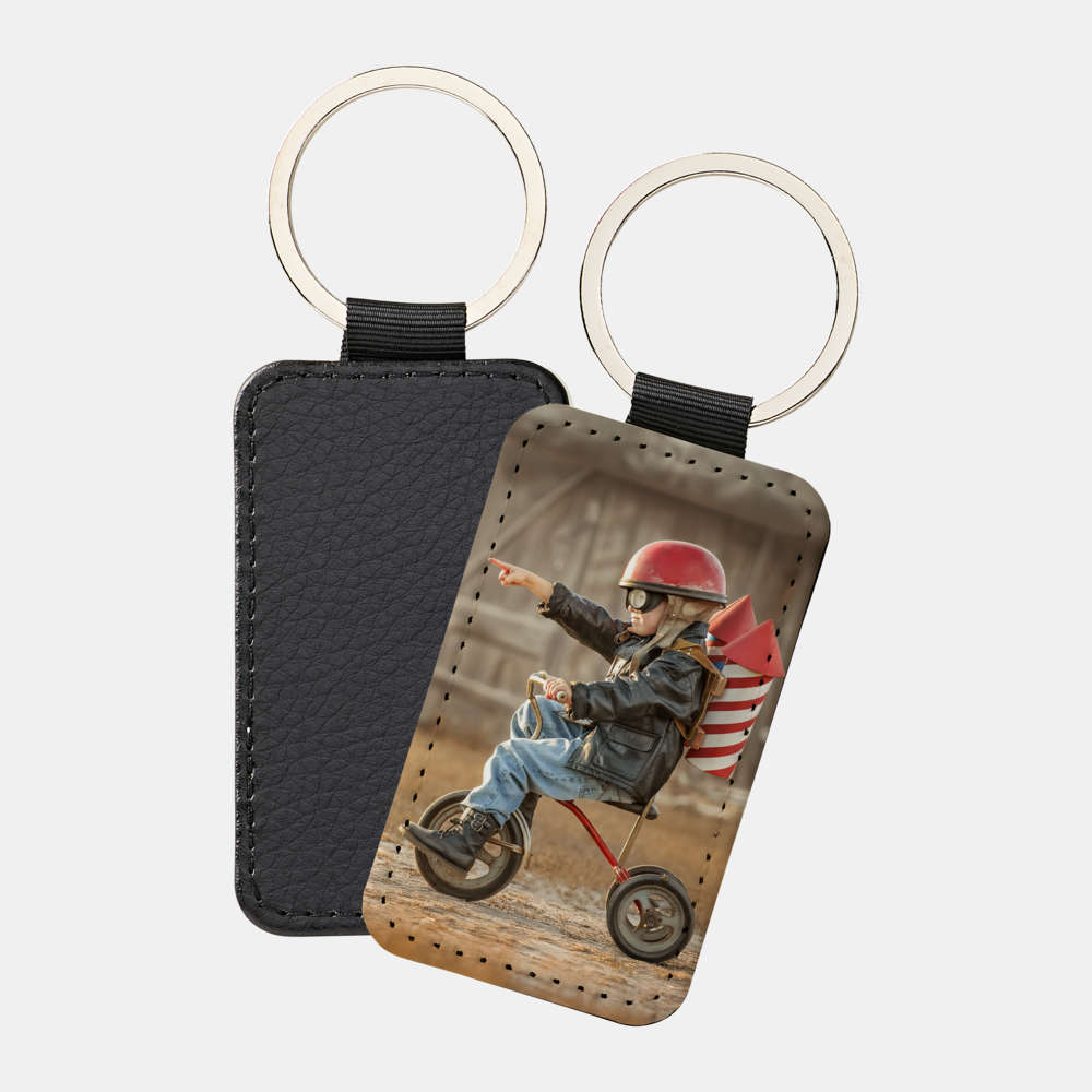 Ein rechteckiger Schlüsselanhänger zeigt ein Kind mit Helm auf einem Dreirad und Raketenrucksack.